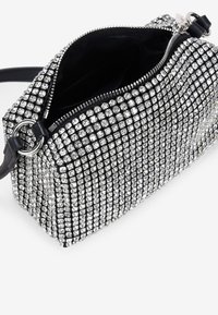 Bolso de mano negro cubierto de pequeños cristales de rhinestone transparentes. Cuenta con un cierre de cremallera y una correa desmontable. Diseño texturizado y geométrico.