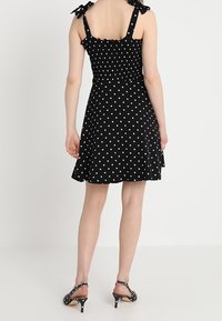 Czarna sukienka w kropki z marszczeniem na górze i regulowanymi ramionkami. Rozkloszowana spódnica oraz eleganckie wysokie obcasy z paskami na kostkach.