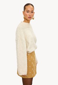 Suéter crema y esponjoso de mangas largas combinado con una falda texturizada dorada con adornos plateados y un diseño ajustado.