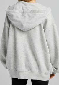 Sudadera con capucha gris de textura suave, con hombros caídos y dobladillo acanalado. Presenta una capucha amplia y un ajuste casual.