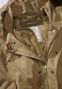 Parka beige con chiusura a zip e bottoni. Presenta una fodera interna, cappuccio con coulisse e etichette di marca all'interno. Nessuna tasca esterna visibile.
