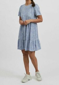 Blå kortärmad klänning med ett lager av volanger, mönster av små vita prickar och en avslappnad passform, parat med vita sneakers.