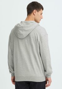 Sweat à capuche gris clair en tissu doux, doté d'une capuche avec cordon de serrage, de poignets côtelés et d'une coupe décontractée. Le dos présente un motif simple.