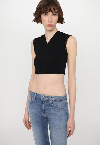 Black cropped top with scalloped edges, V-neck design, and short sleeves, paired with light blue fitted jeans.