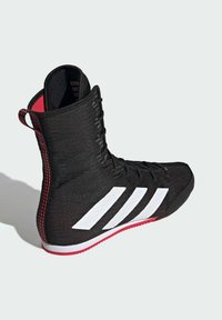 Black athletic shoe with a high-top design, featuring white stripes and red accents. Textured fabric and a lace-up front for secure fit.