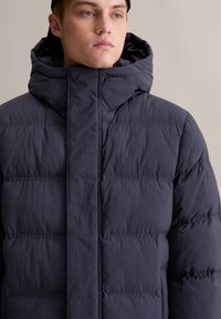 Marineblauer Pufferjacke mit hohem Kragen und Kapuze. Hergestellt aus leichtem Stoff, mit gestepptem Design und einem Frontreißverschluss.