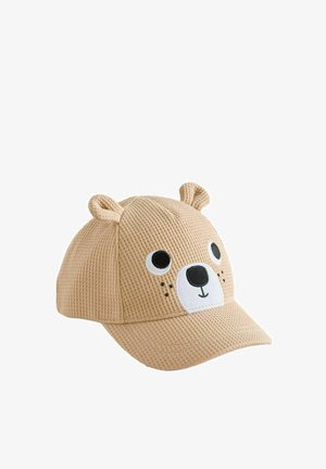 Bonnet beige en maille gaufrée avec visage d’ours, yeux noirs et blancs, nez noir, bouche souriante et petites oreilles en tissu sur le dessus.