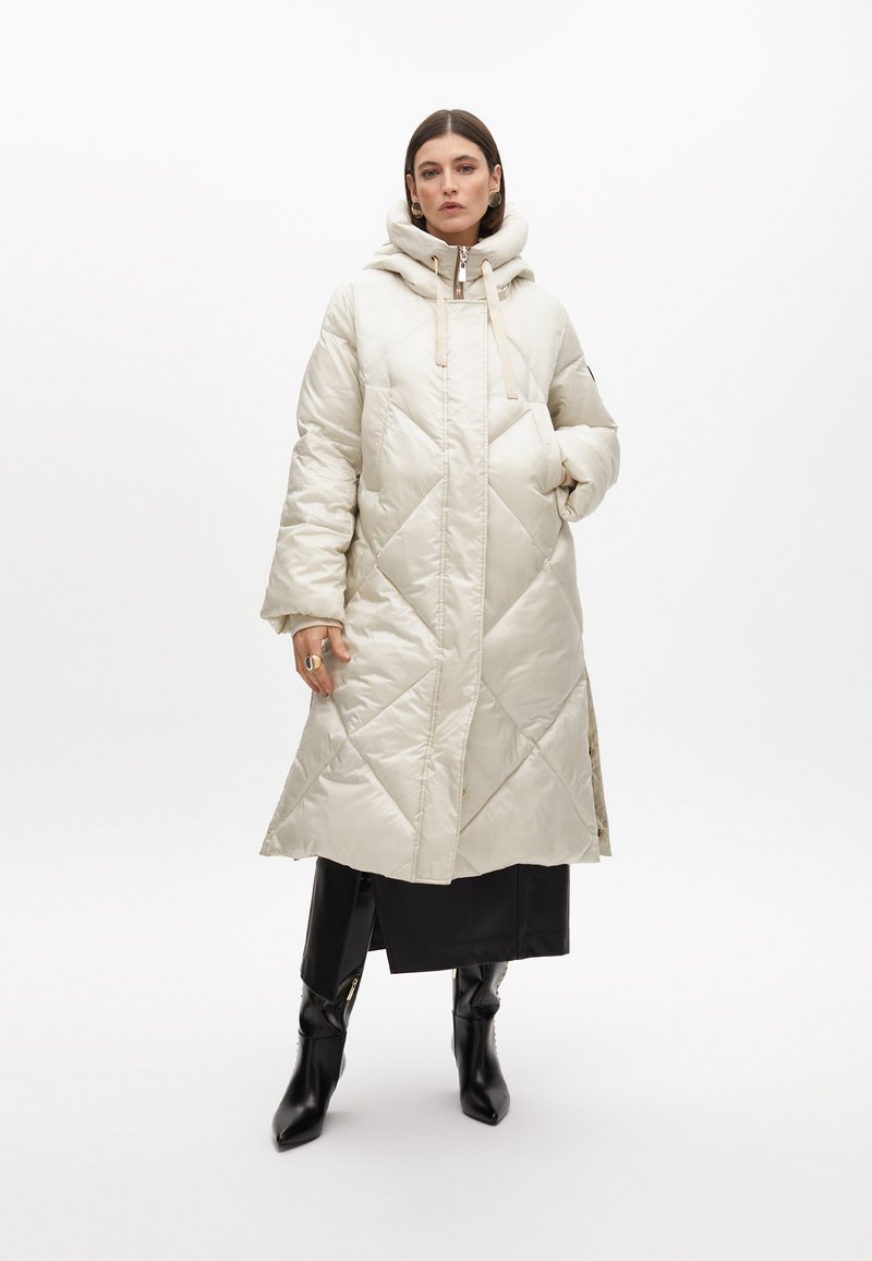 Beige kviltad lång jacka med huva, som har diamantmönstrad söm, sidofickor och dragkedjestängning fram.