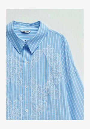 Chemise bleu clair à manches longues avec des rayures verticales blanches et des volutes brodées blanches complexes, fermeture à boutons sur le devant et col pointu.