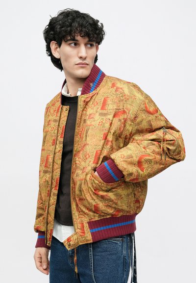 Bomber bunda zo zlatého materiálu s jemnými červenými vzormi. Má rebrované bordové a modré manžety, predný zips a bočné vrecká.