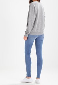 Felpa grigia con polsini e orlo a coste, abbinata a jeans skinny azzurri chiari e sneaker bianche, vista da dietro.