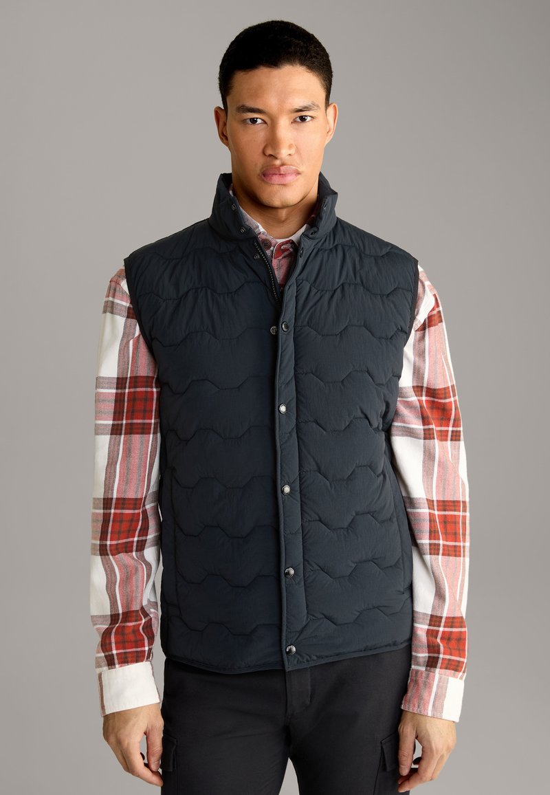 Marineblauer gesteppter Weste mit hohem Kragen, ausgestattet mit einer vorderen Druckknopfverschluss und strukturiertem Muster, getragen über einem karierten rot-weißen Hemd.