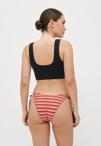 Črn bikini vrh s kvadratnim izrezom, v kombinaciji z rdečimi in belimi črtastimi bikini hlačkami, ki imajo stranske zaveze in nabran teksturo na hrbtni strani.