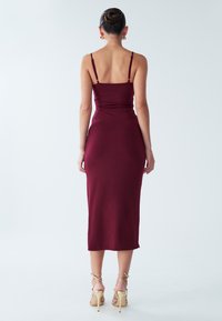 Bordo spalvos prigludusi midi suknelė su plonomis reguliuojamomis petnešėlėmis, kūną apgaujančios formos ir lygiu audiniu, derinama su aukštakulnėmis basutėmis su dirželiais.