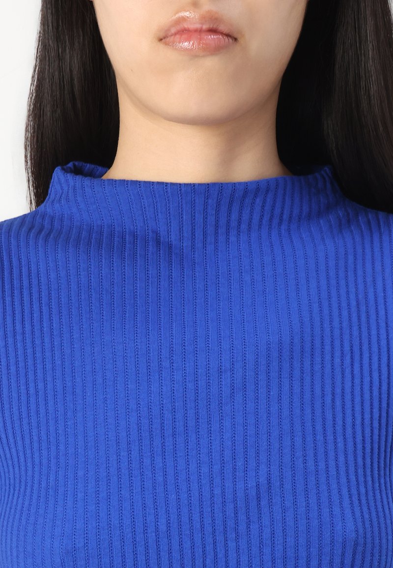 Rippenshirt in Blau mit hohem Kragen. Der Stoff wirkt glatt, hat vertikale Streifen und sitzt eng am Hals und an den Schultern.