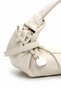 Kremowa, miękka skórzana torba na ramię o zebranym designie, z regulowanym paskiem i metalowym detalem w postaci zawieszki. Gładka tekstura i minimalne zdobienia.