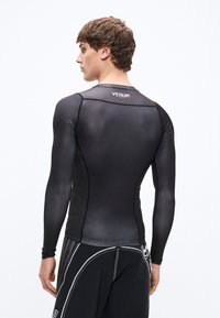 Czarna, dopasowana koszulka ochronna z długim rękawem, gładką fakturą i logo Venum na górnej części pleców. W komplecie czarne spodenki z białymi akcentami.