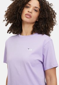 T-shirt in cotone viola chiaro con scollo a girocollo, maniche corte e un piccolo logo FILA ricamato in bianco e blu navy sul petto.