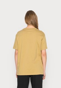 T-shirt med kort ärm, rund hals i en ljusbrun färg, tillverkad av bomull, med en avslappnad passform och minimal sömnadsdetaljering.