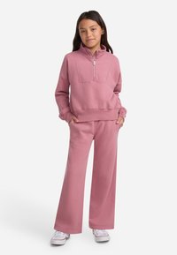 Rosa genser med høy krage og halv glidelås, kombinert med matchende brede bukser. Stoffet ser mykt ut med en glatt tekstur.