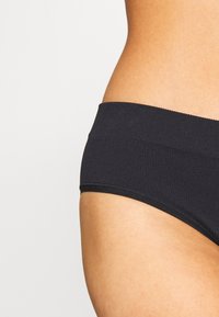 Sous-vêtements hipster en tissu noir côtelé avec une large ceinture lisse et des bords sans couture pour le confort. La texture semble douce et extensible.