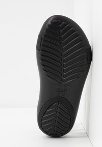 Musta kumipohja, jossa on teksturoitu herringbone-kuvio, varustettuna kohokuvioiduilla logoilla ja koko-tiedoilla, valkoista taustaa vasten.