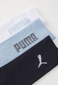 Conjunto de tres diademas acanaladas en blanco, azul claro y azul marino. Presenta el logo "PUMA" en negro y una silueta gráfica en blanco en la diadema azul marino.