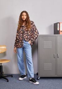 Camisa negra de botones con estampado floral, corte holgado; jeans de tiro alto azul claro; zapatillas negras con suelas blancas; taquilla gris al fondo.