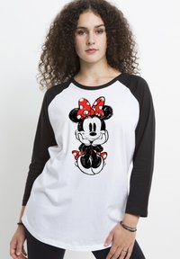 T-shirt bianco con maniche raglan nere, caratterizzato da un fiocco a pois rossi e un'illustrazione di un personaggio dei cartoni animati sul davanti. Tessuto morbido.