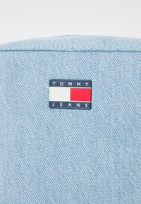 Una tela de mezclilla azul claro con un tejido texturizado presenta un parche rectangular etiquetado como "TOMMY JEANS" en colores marino, blanco y rojo.