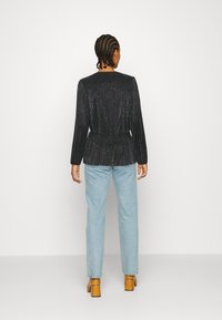 Camisola preta com glitter e mangas longas, com uma cintura peplum, combinada com jeans de perna reta azul clara e sapatos de salto bloco castanhos.