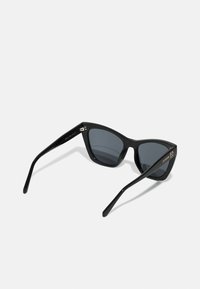 Occhiali da sole cat-eye neri con lenti grigie, finitura lucida, aste sottili e dettaglio logo dorato sulla manica sinistra.