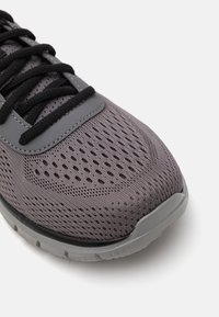 Sport shoe with a grey mesh upper, featuring perforations for breathability, black laces, and a cushioned grey sole.
