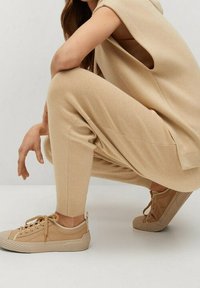 Beige gestricktes ärmelloses Oberteil kombiniert mit passenden schmal geschnittenen Hosen, beide mit gerippten Bündchen; hellbraune Sneakers mit strukturierten Sohlen.