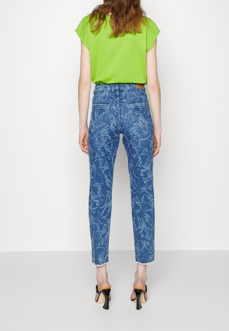 Haut vert à manches courtes associé à un jean denim taille haute orné d'un motif floral et d'un ourlet effiloché, complété par des sandales noires à talons.