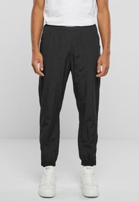 Schwarze Hosen mit elastischem Bund aus leichtem Stoff, mit schmal zulaufendem Schnitt und gekrempelten Beinenden, getragen mit weißen Turnschuhen.