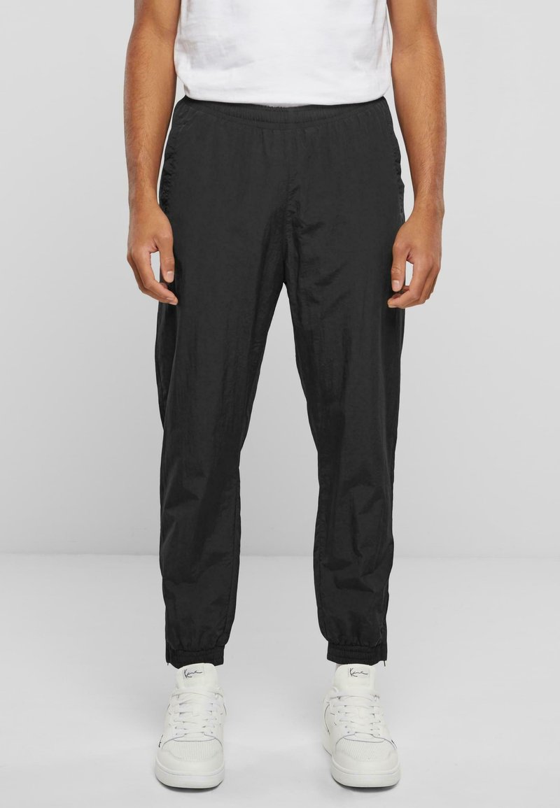 Schwarze Hosen mit elastischem Bund aus leichtem Stoff, mit schmal zulaufendem Schnitt und gekrempelten Beinenden, getragen mit weißen Turnschuhen.