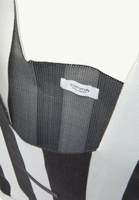 Schwarz-weiß gestreifte Tragetasche mit einer strukturierten Oberfläche und einem Stoffetikett im Inneren. Verfügt über eine abgerundete Oberseite und ein offenes Design.