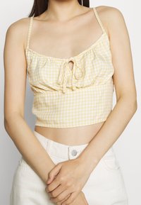 Yellow and white checkered crop top with adjustable spaghetti straps, gathered front with a tie, made from lightweight fabric.