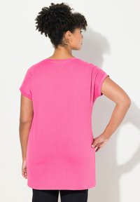 Růžové bavlněné tričko s krátkými rukávy, volný střih a zakulacený spodní lem. Zobrazeno ze zadní strany na světlém pozadí.