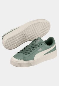 Green leather sneakers with textured white rubber sole, scalloped edge, classic lace-up design, and white logo detail on side.