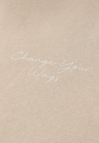 Tissu beige avec texte en cursive blanc indiquant « Change Your Ways » centré sur la surface.