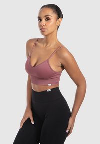 Geribbelde, roze sportbeha met dunne bandjes en een V-hals ontwerp. Gecombineerd met hoge, zwarte leggings met een gebrandmerkte tailleband.