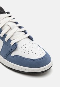 Vit och blå sneaker med perforerad tå, läder och mocka material, platta vita snören och texturerad svart gummisula.