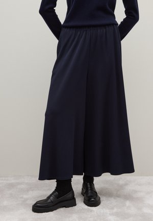 Pantalones de pierna ancha en color azul marino con una cinturilla elástica, hechos de una tela suave, combinados con unos mocasines negros y calcetines oscuros.