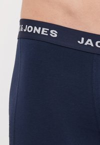 Tamno plave bokserice od mekog, rastezljivog materijala. Imaju široki elastični pojas s natpisom "JACK & JONES" u bijeloj boji. Vidljivi detalji šavova.