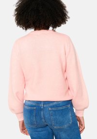Pull en maille douce rose clair avec manches longues bouffantes et col haut, associé à un jean denim bleu avec poches arrière.