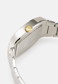 Silver metal wristwatch featuring a rectangular case, yellow crown, and link bracelet. Smooth finish with subtle branding on the back.