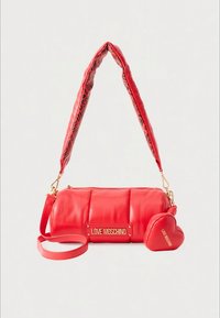 Mala de mão em couro vermelho com textura almofadada, ferragens douradas e um pendente destacável em forma de coração. Apresenta uma alça com padrão e uma placa de logótipo.