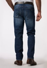 Vaqueros de mezclilla azul para hombre con un diseño de pierna recta, cinco bolsillos, un ligero desgaste y una textura suave, combinados con zapatos de cuero marrón.